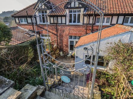 Metal gate and stone steps leading down to a patio with table and chairs outside a brick and white cottage at Trackside Ruswarp