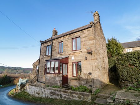 A stone cottage with a small porch and multiple windows beside a narrow road at Providence Cottage in Ugglebarnby near Sleights