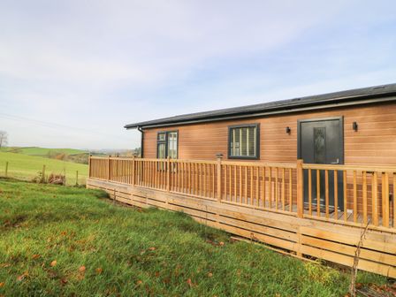 A wooden cabin with black trim and a wooden railing on a grassy field at Seren Lodge in Builth Wells