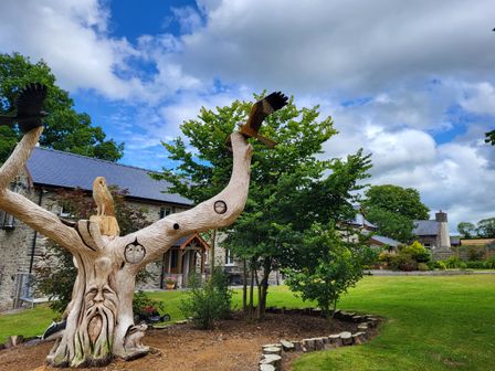 A garden with a carved wooden tree sculpture and stone houses in the background at Teifi Cottage Cardigan Near Cenarth