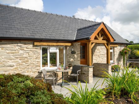 A stone cottage with a slate roof and wooden porch with two chairs and a table on the patio at Gwaun Cottage in Cardigan Near Cenarth