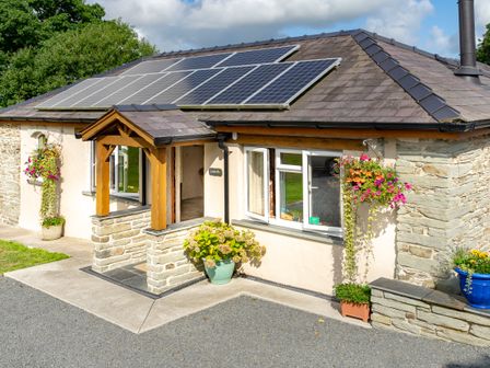 A single story cottage with solar panels on the roof and flowers in pots at Cothi Cottage Cardigan Near Cenarth