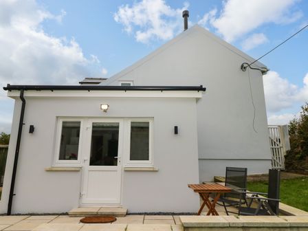 Exterior view of a white house with a door and two windows a small table and two chairs on a patio at Orchard View Pembroke
