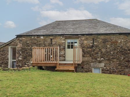 A stone building with a wooden balcony and steps on a grassy area at Logan Barn in Poldue near Camelford