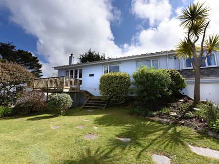 A front yard with grass shrubs a wooden deck and a white house with garage at Northern Lights in Polzeath