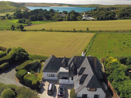 An aerial view of a house with multiple cars in the driveway surrounded by fields and trees near a body of water at Seaworthy in Daymer Bay