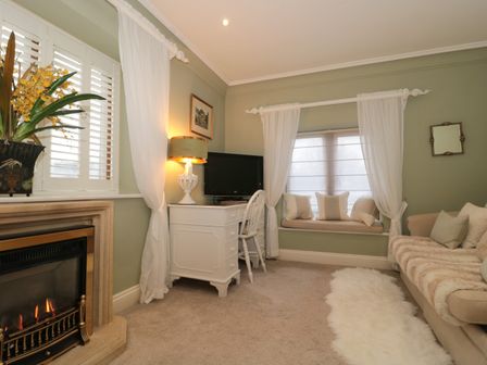 A living room with a fireplace a white desk and chair a sofa with cushions and a window seat at Tree Tops in Broadway