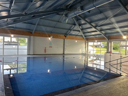 A swimming pool with windows and safety equipment at Satinwood in White Cross near Newquay