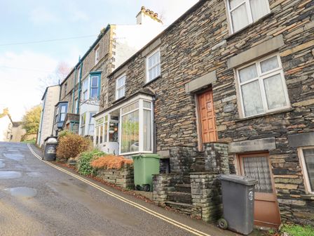 A row of stone and brick houses along a sloping street with windows doors and trash bins