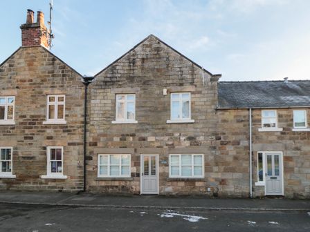 A stone facade of a residential building with multiple windows and two front doors