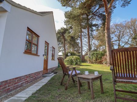 A garden with wooden chairs and a small table with two mugs outside a white house at West End in Martlesham Village