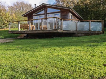 A wooden house with a glass railing balcony and outdoor furniture on a grassy slope at 3 Hedgerows in Lanreath