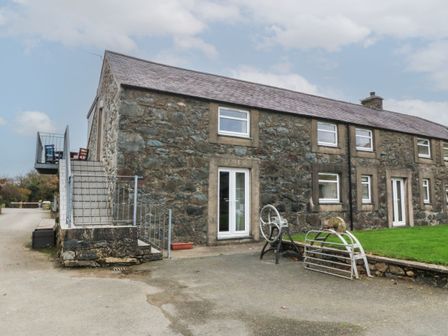 A stone building with multiple windows and doors a metal staircase on the left and a grassy area on the right at Cwellyn in Pwllheli