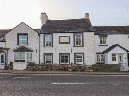 Exterior view of white stone cottages with grey roof and multiple windows along a street