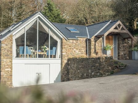 A stone house with large glass windows showing a dining table and chairs at Leeward Cottage in Cosheston near Pembroke Dock