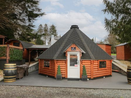 A wooden cabin with a black hexagon shingle roof a white door and two potted plants on a deck at The Hideaway in Dungiven Londonderry