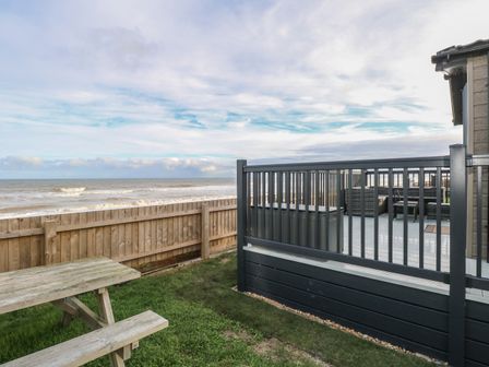 A wooden picnic table on grass near a fenced patio overlooking the ocean at Dorchester in Broomholm near Mundesley