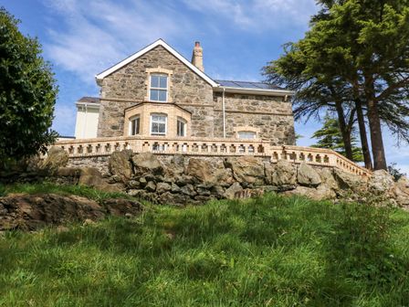 A stone house with a brick terrace and green grass in the foreground at Fir Grove in Menai Bridge