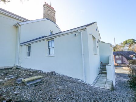 The exterior side view of a white building with steps leading to a door and gravel ground at The Fir Grove Annex in Menai Bridge