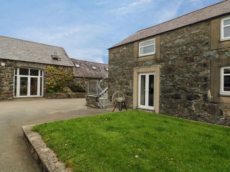 An outdoor courtyard with two stone buildings and a small patch of grass at Dinas near Pwllheli