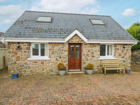Stone house with two windows wooden door potted plants and bench on paved ground at Trevone Goodwick
