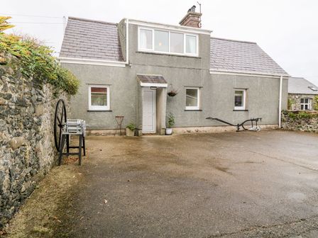 The exterior of a two-story house with a grey roughcast finish a small porch a paved area and stone walls at Y Bwthyn Llannor near Pwllheli