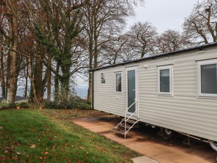 A white mobile home with stairs on a paved area near trees at 6 Manor Park in Bucks Cross