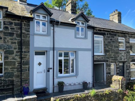 A row of stone and white painted terraced houses with small fenced front gardens and a blue flower pot at Gwelfor in Harlech