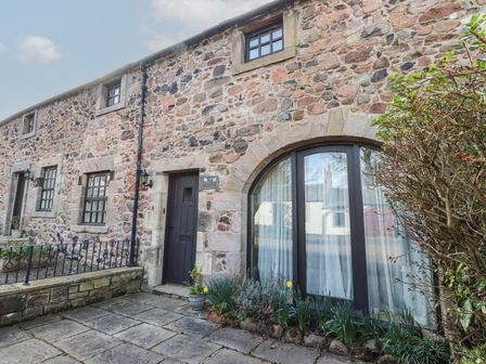 Stone exterior of a building with a door and arched window surrounded by plants at Primula Patch in Akeld near Wooler