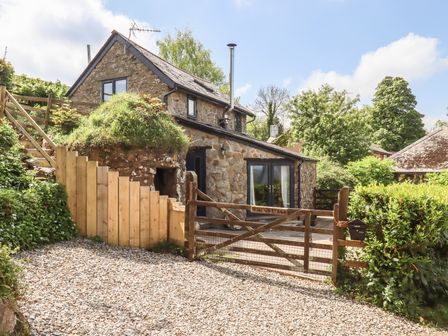 A stone cottage with wooden gate gravel driveway and green plants at Ash Cottage in Chagford