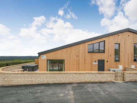 A wooden exterior of a building with a stone wall and a hot tub in a backyard at Bears Court Barn 1 Little Rissington near Bourton-On-The-Water