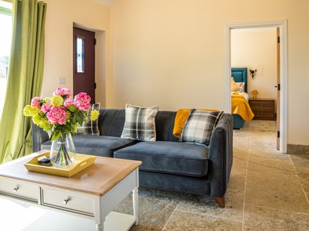 A living room with a blue sofa pillows and a coffee table with flowers at Bears Court The Annex Little Rissington near Bourton-On-The-Water