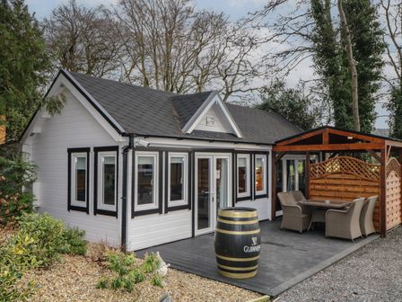 A small white house with black window frames a patio with a wooden pergola and outdoor dining furniture at Drumrane Lodge in Dungiven Londonderry