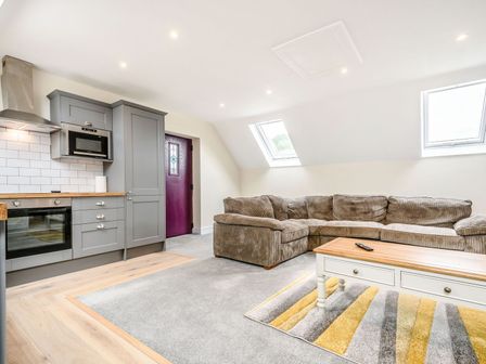 A living area with a sectional sofa coffee table and kitchen cabinetry with appliances at Bears Court The Flat in Little Rissington near Bourton-On-The-Water