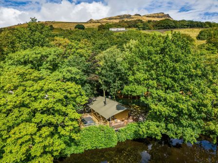 A safari tent surrounded by trees near a body of water at The Kingfisher Safari Tent in Greenfield