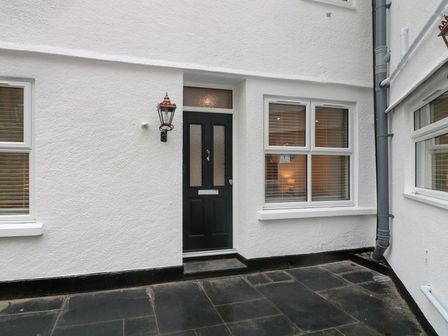A black front door with windows on either side and a wall-mounted lamp in a white exterior at Denning Cottage in Dartmouth