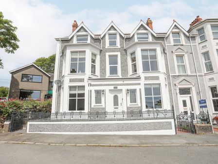 The front view of a residential building with multiple windows and a white entrance door at Llwyn Onn 2 bed in Criccieth