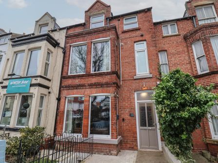 A red brick residential building with large windows and a front door surrounded by plants and a small fence at North Bay Guest Accommodation in Scarborough
