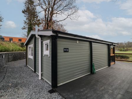 An exterior view of a small green building with white trim windows and a black deck at The Roe in Dungiven Londonderry