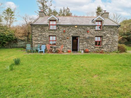 A stone house with red windows and outdoor chairs on grass at Mudflat in Toormore near Schull County Cork