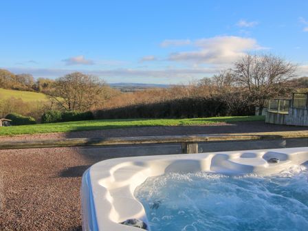 An outdoor hot tub bubbling with water overlooking a grassy area and distant trees and hills at Hillview in Stottesdon near Cleobury Mortimer