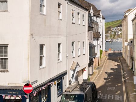 A narrow street with white buildings on either side leading to a marina with boats and green hills in the background at Sunnyhaven in Dartmouth