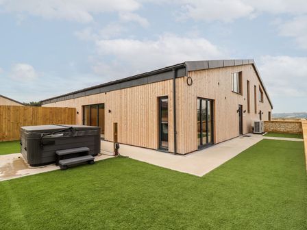 A wooden house exterior with a hot tub on artificial grass at Bears Court Barn 3 Little Rissington near Bourton-On-The-Water