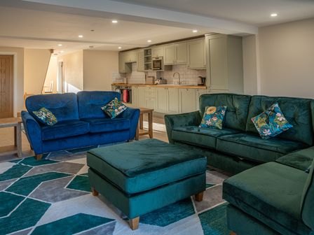 A living room with green and blue sofas and a kitchen area in the background at Bears Court Barn 5 in Little Rissington near Bourton-On-The-Water