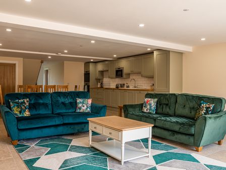 A living room with two green sofas a wooden coffee table and kitchen cabinets at Bears Court Barn 6 Little Rissington near Bourton-On-The-Water