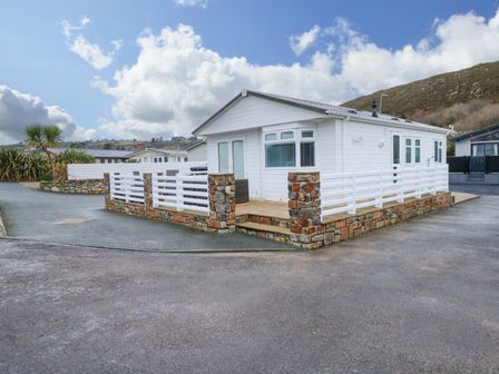 A white single-story house with a stone and white fence surrounding a patio at Un Diwrnod One Day The Warren T22 The Warren near Abersoch