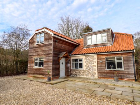 A two-story house with wooden exterior panels and red tiled roof with a stone and paved front yard at Natterjacks in Syderstone