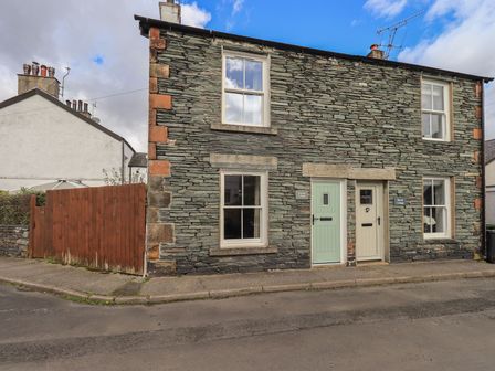 A stone exterior cottage with two doors and four windows beside a wooden gate at Capella Cottage in Keswick