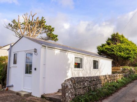 The exterior of a white single-story building with a stone wall along a narrow road at Fifty Degrees North in St Just