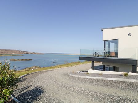 A modern house with glass balcony overlooking a body of water and a gravel driveway at Atlantic Sea Breeze Near Gortahork County Donegal